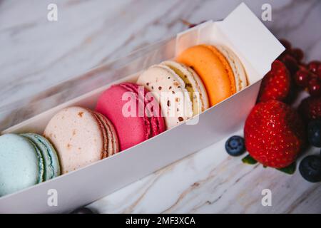 Macaronis in una scatola bianca con una finestra trasparente. Colore dessert, rosa, menta, macaroon blu e arancio. Fragole, lamponi, mirtilli e f Foto Stock