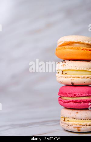Rosa Macaron, arancione e beige, blu su marmo. Dessert francese uno sopra l'altro, appetitoso, dieta Foto Stock