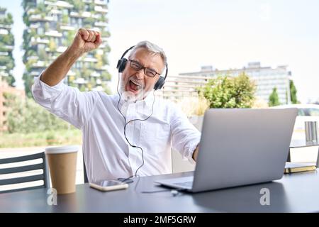 Felice uomo d'affari anziano che utilizza un notebook per celebrare i risultati vincenti online. Foto Stock