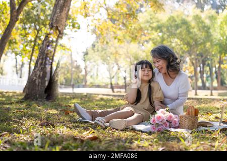 Felice nonna asiatica picniching con la sua bella nipote in parco insieme. concetto di svago e famiglia Foto Stock