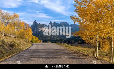 Autumn Mountain Road - una vista serale autunnale di una strada di campagna che si estende verso aspre creste di montagna. Wull Creek Pass Road, Colorado, Stati Uniti. Foto Stock