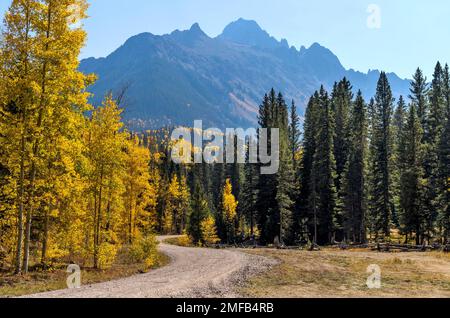 Autumn Mountain Road - Una strada per il backcountry che si snoda in una valle colorata alla base dell'aspra gamma Sneffels in un soleggiato pomeriggio di ottobre. Ridgway, Colorado, Stati Uniti. Foto Stock
