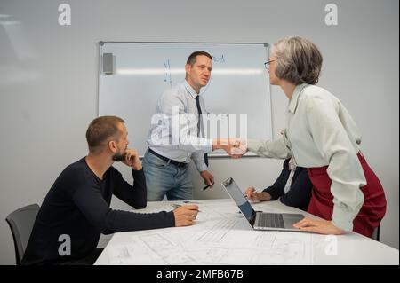 Il capo fa una presentazione ai subordinati alla lavagna bianca. Uomo caucasico che scuote le mani con donna di mezza età. Foto Stock