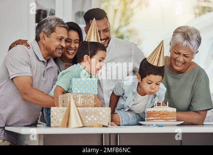 Compleanno, celebrazione e bambini gemelli con la famiglia che soffia le candele su una torta al loro partito. Felici, eccitati e bambini con i loro genitori e. Foto Stock