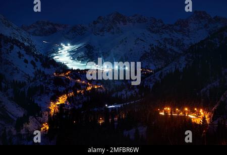 Paesaggio di strada incandescente da Medeu pattinaggio su ghiaccio a Shymbulak stazione sciistica a Tian Shan montagne durante la notte nella città di Almaty, Kazakistan Foto Stock