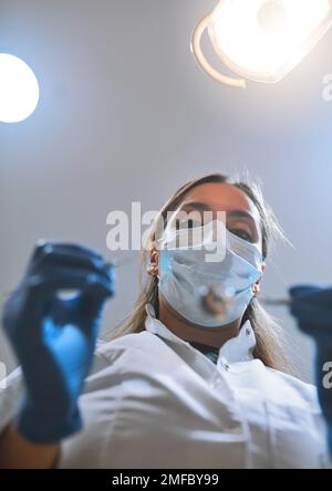 Questo non danneggia affatto. Ripresa pov ad angolo basso di una giovane dentista focalizzata che indossa una maschera chirurgica mentre tenta di lavorare sui denti di un paziente. Foto Stock