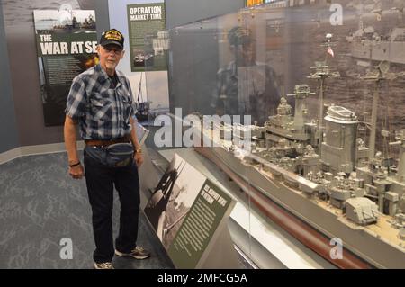 Virgil Greene, che ha servito a bordo della USS Newport News (CA 148) come tecnico della caldaia di seconda Classe, fornisce alcune informazioni riguardo al suo servizio durante una visita al Museo Navale di Hampton Roads. Greene ha servito a bordo di Newport News dal 1969-1973 durante la guerra del Vietnam, ed è raffigurato con un grande modello dell'incrociatore. Il grande modello di nave è in mostra al museo come parte della loro mostra “la guerra dei Temila giorni in mare: Gli Stati Uniti Navy in Vietnam, 1950-1975.” Il museo si trova al secondo piano dell'edificio Nauticus nel centro di Norfolk, Virginia. Foto Stock