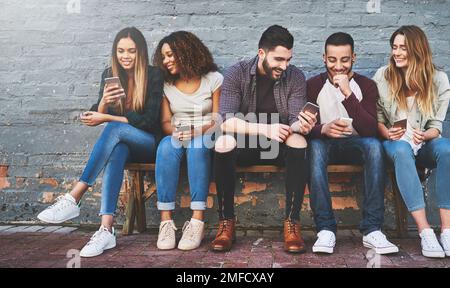 Come i millennial trascorrono il loro tempo freddo. Online. un gruppo di giovani amici che usano il loro cellulare all'aperto. Foto Stock