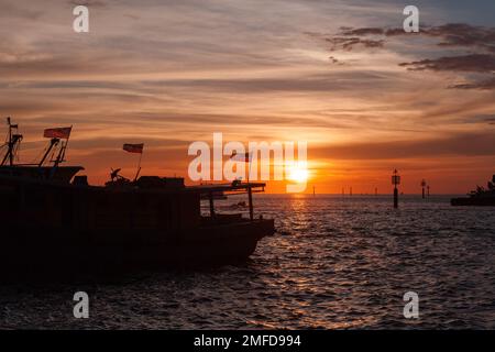 Silhouette di barche da pesca con bandiere malesi ormeggiate al KK Fish Market al tramonto Foto Stock