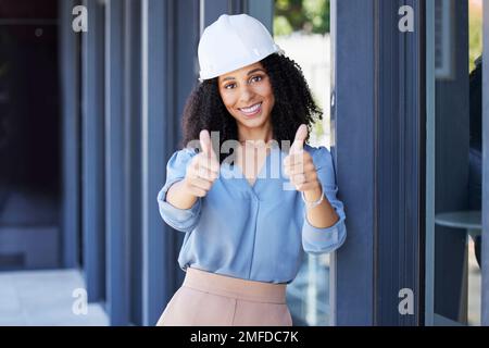 Donna nera, ritratto sorriso e pollici in su per la costruzione, costruzione o buon lavoro con elmetto per la sicurezza sul lavoro in loco. Felice afro americano femmina Foto Stock