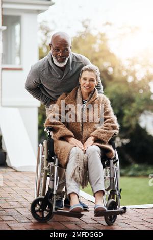 Stavamo trascorrendo la nostra giornata all'aperto oggi. un uomo anziano che spinge la moglie in sedia a rotelle intorno al cortile a casa. Foto Stock