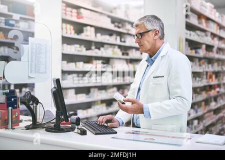 Questo è il migliore per l'influenza. un farmacista maschio maturo messo a fuoco che scrive su una tastiera del calcolatore mentre tiene una scatola del farmaco. Foto Stock