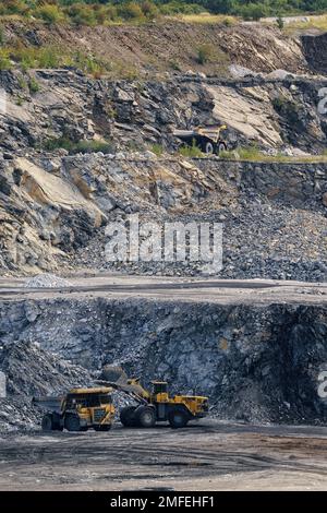 Caricare la pietra con una pala caricatrice gommata su un autocarro con cassone ribaltabile. Estrazione di pietra nella cava. Foto Stock