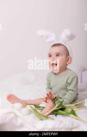 cute bambino con orecchie di coniglio sulla sua testa e tulipani a casa sul letto. Concetto di Pasqua. Foto di alta qualità Foto Stock