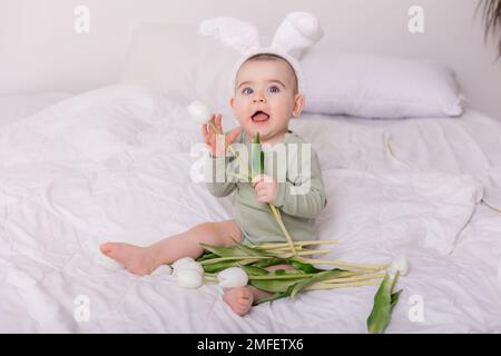 cute bambino con orecchie di coniglio sulla sua testa e tulipani a casa sul letto. Concetto di Pasqua. Foto di alta qualità Foto Stock