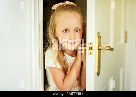 Okay, mi hai trovato. Ritratto di una ragazza allegra che apre una porta mentre guarda la fotocamera a casa. Foto Stock