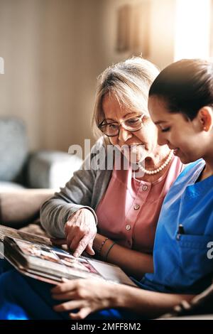 Visitare vecchi ricordi. un'infermiera e una donna anziana che guardano insieme un album fotografico. Foto Stock