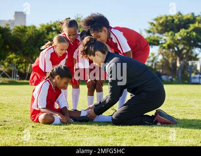 Incidente, infortunio e bambini squadra di calcio con il loro allenatore in una huddle aiutare una ragazza atleta. Sport, primo soccorso e bambino con una ferita, dolore o muscolo Foto Stock