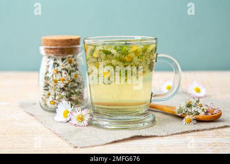 Pianta medicinale a base di erbe essiccata Daisy comune, noto anche come Bellis perennis. Fiori secchi in vaso di vetro e tè alle erbe in vetro, all'interno. Foto Stock