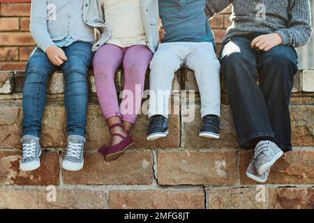 Soggiorno a scuola. bambini della scuola elementare irriconoscibili seduti su una parete di mattoni all'esterno. Foto Stock
