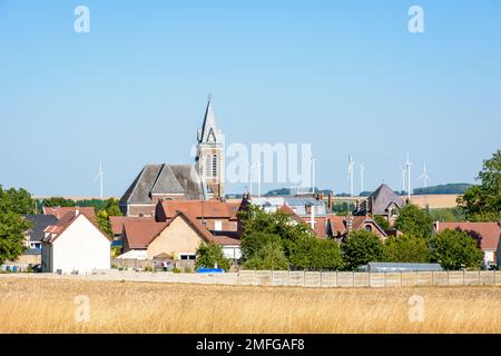 Vista sul piccolo villaggio rurale di Vendeuil, Francia, e il suo campanile, circondato da campi coltivati, con turbine eoliche sullo sfondo. Foto Stock