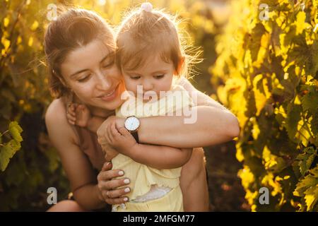 Donna contadina con bambino figlia che cammina tra le file con viti. Concetto di vendemmia del vino. Foto Stock