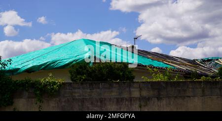 tetto casa riparazione temporanea su tetto gravemente danneggiato tempesta con un grande foro di perdita in scandole e tetto coperto foro con verde di plastica tarp Foto Stock