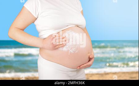 Colpo corto di una donna incinta con l'abbronzatura sul suo ventre sullo sfondo dell'oceano Foto Stock