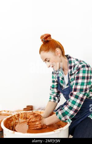 Allegra scultore femminile mentre lei fa pentola di argilla su ruota di ceramica. Idea di piccola impresa e imprenditorialità. Hobby domestico, intrattenimento e leisur Foto Stock