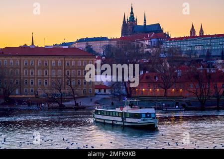 La barca passeggeri sul fiume Moldava e il quartiere di Mala Strana con il castello di Praga al crepuscolo sullo sfondo, in Cechia Foto Stock