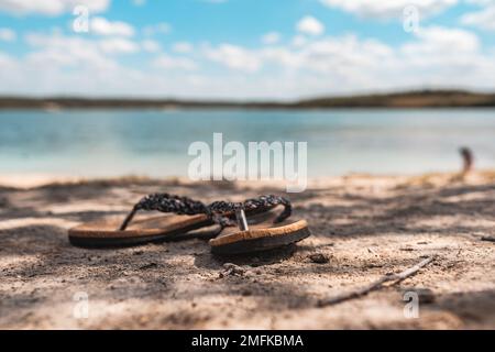 Un paio di pantofole sulla sabbia della spiaggia con uno sfondo sfocato Foto Stock