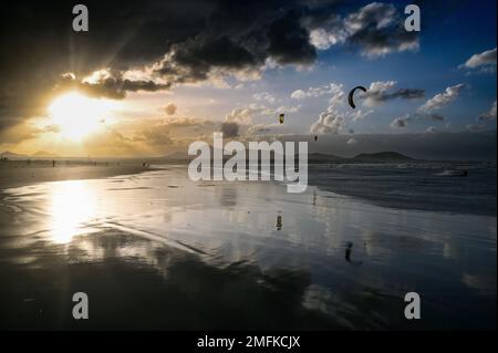 Kitesurfers sulla spiaggia di Caleta de Famara, Playa de Famara, a Lanzarote al tramonto. Foto Stock