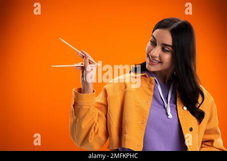 Giovane donna brunette guardando bacchette di bambù isolato su arancione, immagine stock Foto Stock