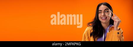 Giovane donna che tiene bacchette di bambù e winking isolato su arancione, banner, immagine stock Foto Stock