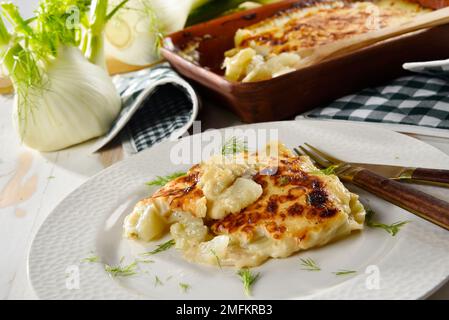 Finocchio al gratin al forno servito in un piatto bianco, con finocchio fresco nelle vicinanze Foto Stock