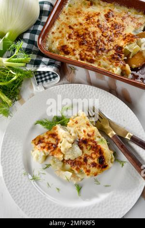 Finocchio al gratin al forno servito in un piatto bianco, con finocchio fresco nelle vicinanze Foto Stock