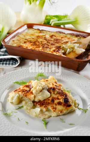 Finocchio al gratin al forno servito in un piatto bianco, con finocchio fresco nelle vicinanze Foto Stock