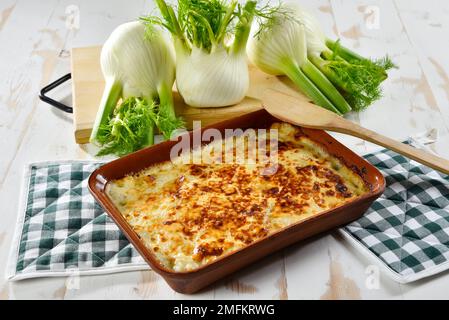 Finocchio al gratin al forno servito in un piatto bianco, con finocchio fresco nelle vicinanze Foto Stock