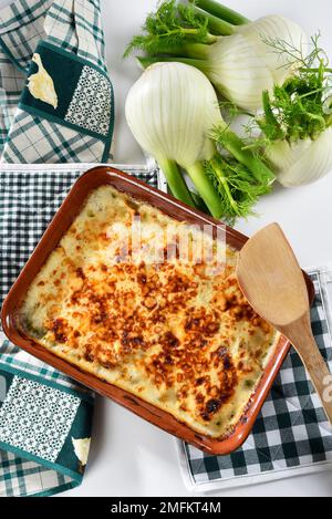 Finocchio al gratin al forno servito in un piatto bianco, con finocchio fresco nelle vicinanze Foto Stock