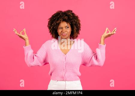 Confuse allegra divertente giovane donna afroamericana in casual si distende le braccia a lato, guarda con un occhio Foto Stock