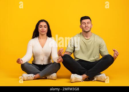 Allegro rilassato giovane donna e ragazzo arabo in casual con gli occhi chiusi sedersi in posizione lotus meditando Foto Stock