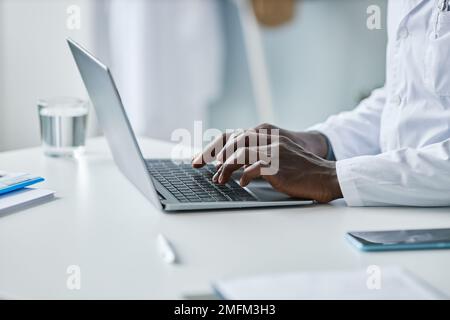 Minimo closeup del medico nero utilizzando il computer portatile in ufficio, concentrarsi sulle mani maschili digitando sulla tastiera, spazio copia Foto Stock