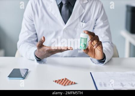 Minimo closeup del medico nero che tiene la bottiglia di pillole e di indicare mentre spiega gli effetti collaterali del farmaco Foto Stock