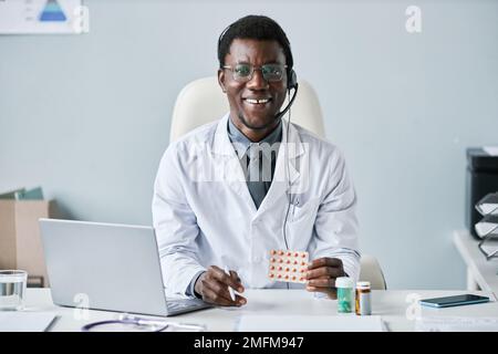 Ritratto di un sorridente medico afroamericano che tiene tablet e indossa cuffie sul posto di lavoro in ufficio Foto Stock