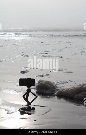 Macchina fotografica per cellulare e cavalletto in spiaggia. Concetto per artista, fotografia all'aperto o riprese, riprese nella natura Foto Stock