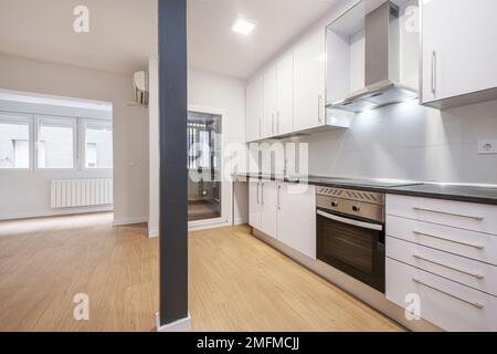 Cucina aperta in camera vuota con colonna di metallo grigio e nuovo armadio da cucina bianco installato con elettrodomestici in acciaio inox integrati e pietra nera Foto Stock