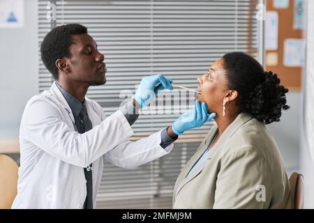 Vista laterale ritratto di giovane medico nero che esamina la donna in clinica e fare controllo della gola Foto Stock