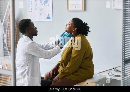 Vista laterale ritratto di giovane medico nero che esamina la donna in clinica e fare il controllo del collo e della gola Foto Stock