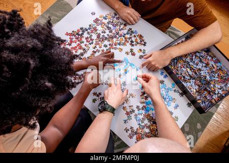 Vista ad angolo alto di una famiglia irriconoscibile che gioca un puzzle insieme a casa. Mettere insieme le cose e risolvere i problemi. Diversità. Foto Stock