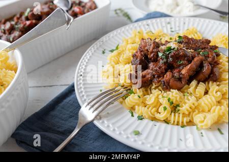 Ragù di pollo o stufato con pasta al burro e parmigiano, su un piatto su fondo di tavola di legno bianco Foto Stock